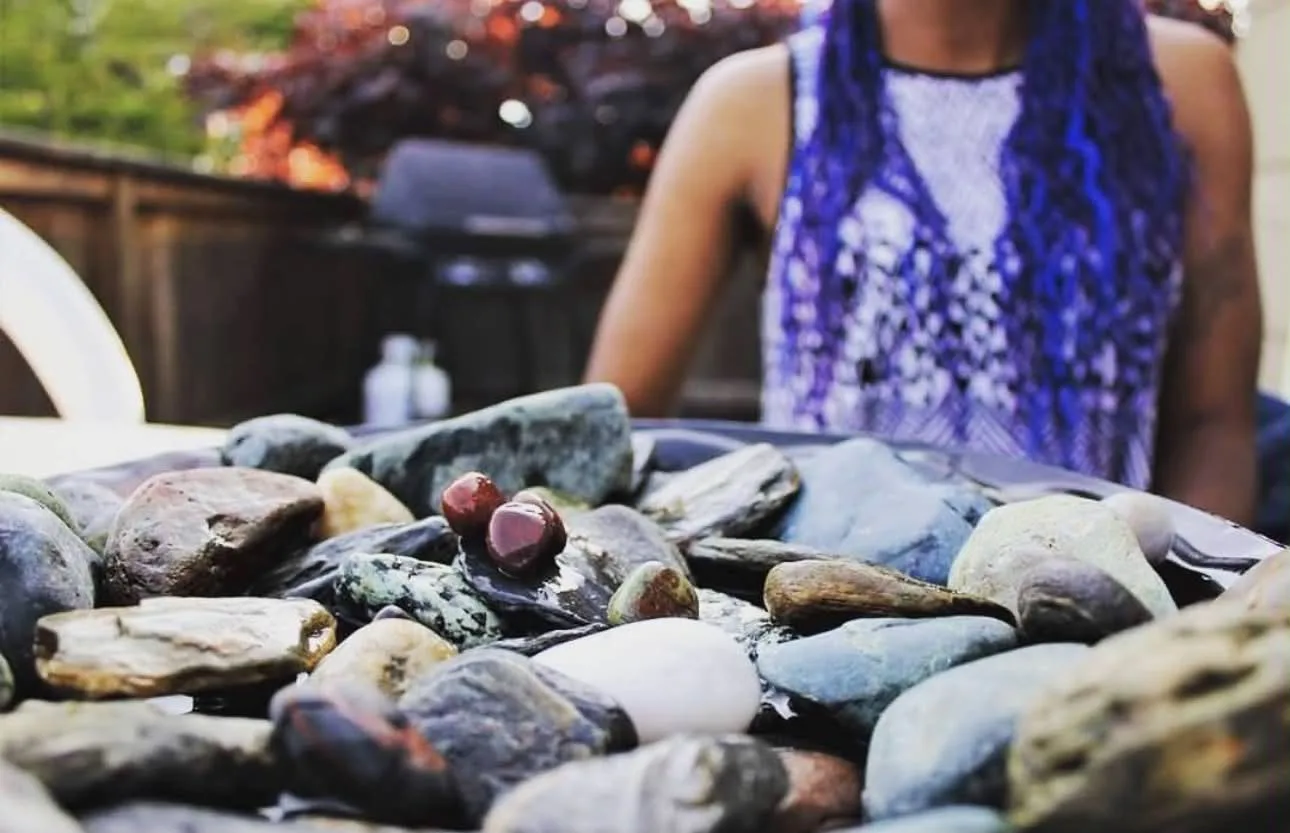 A bowl of smooth river stones in focus, Paula sitting behind them in the garden